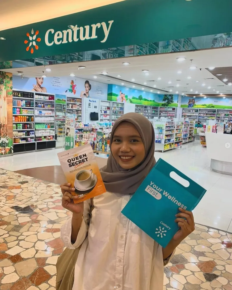 Pelanggan QSC memegang kemasan Queen Secret Coffee dan tas belanja di depan apotek Century dalam mall